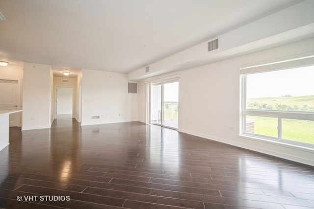 unfurnished living room with plenty of natural light, dark wood-style floors, visible vents, and baseboards