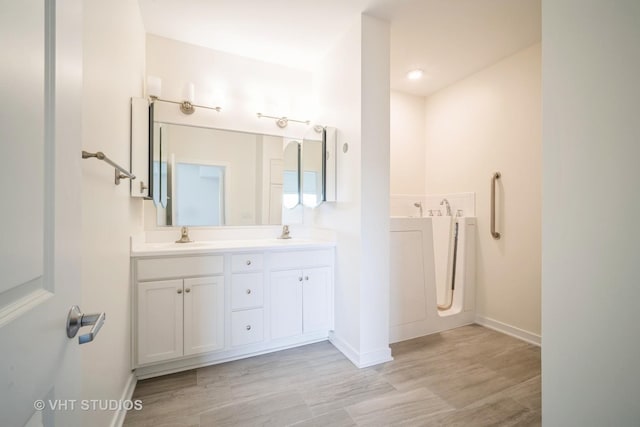 bathroom featuring double vanity, baseboards, wood finished floors, and a tub