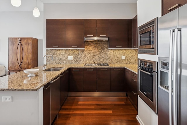 kitchen featuring a sink, under cabinet range hood, appliances with stainless steel finishes, a peninsula, and decorative backsplash