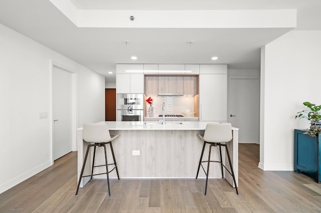 kitchen featuring decorative backsplash, light countertops, modern cabinets, and light wood-type flooring