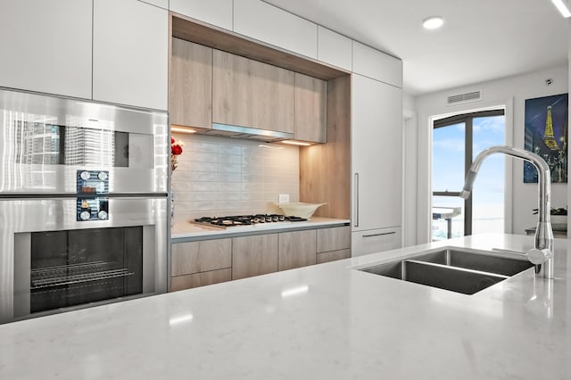 kitchen featuring visible vents, stainless steel appliances, a sink, modern cabinets, and backsplash