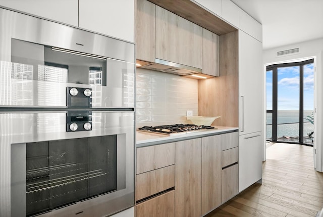 kitchen with tasteful backsplash, light brown cabinetry, hardwood / wood-style floors, stainless steel appliances, and modern cabinets