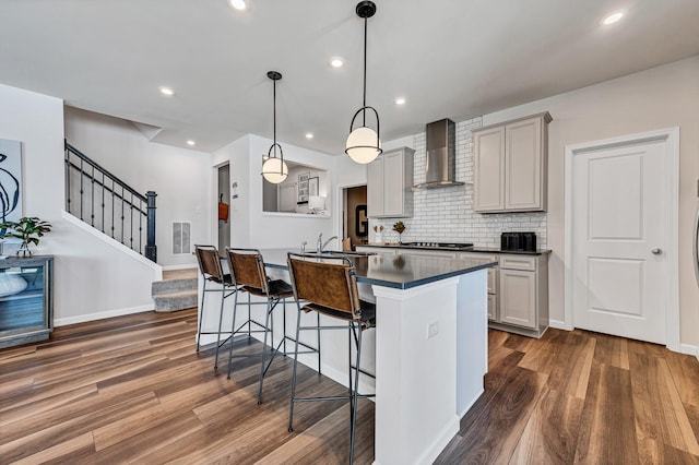 kitchen featuring dark countertops, backsplash, a breakfast bar area, wall chimney exhaust hood, and dark wood-style flooring