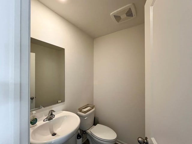 half bath featuring toilet, baseboards, visible vents, and a sink