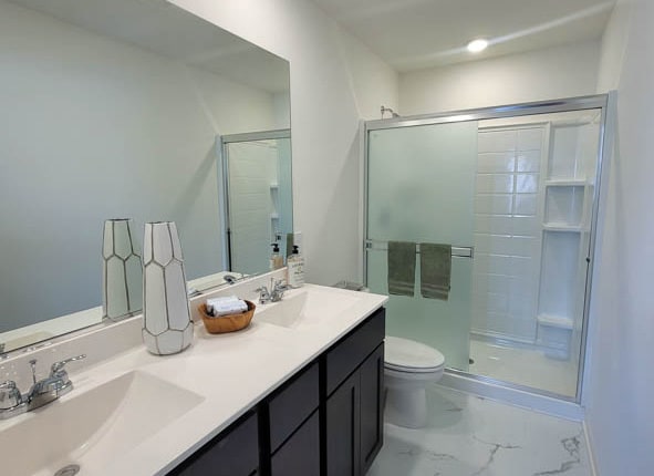 bathroom featuring a sink, toilet, marble finish floor, and a stall shower