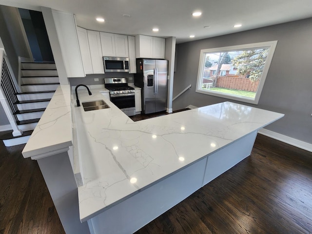 kitchen with light stone counters, a peninsula, stainless steel appliances, and a sink