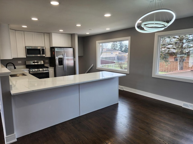 kitchen featuring a sink, light stone counters, a peninsula, stainless steel appliances, and dark wood-style flooring