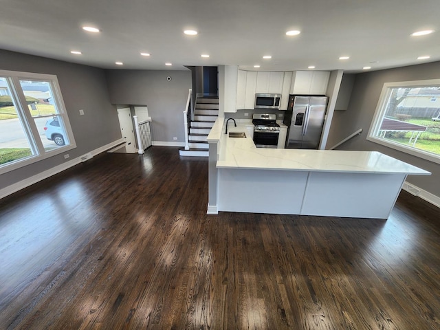 kitchen featuring dark wood-type flooring, a peninsula, stainless steel appliances, white cabinetry, and a sink