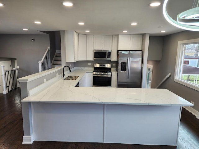 kitchen featuring light stone counters, dark wood-style floors, a peninsula, a sink, and appliances with stainless steel finishes