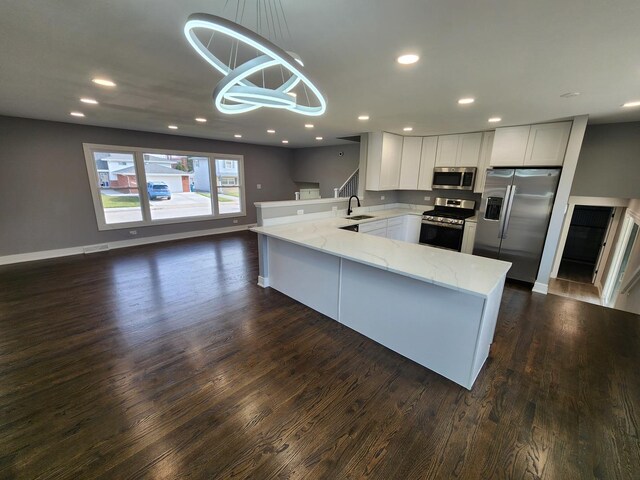 kitchen with a sink, light stone counters, recessed lighting, appliances with stainless steel finishes, and a peninsula