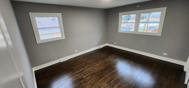 empty room with dark wood-style floors, visible vents, and baseboards