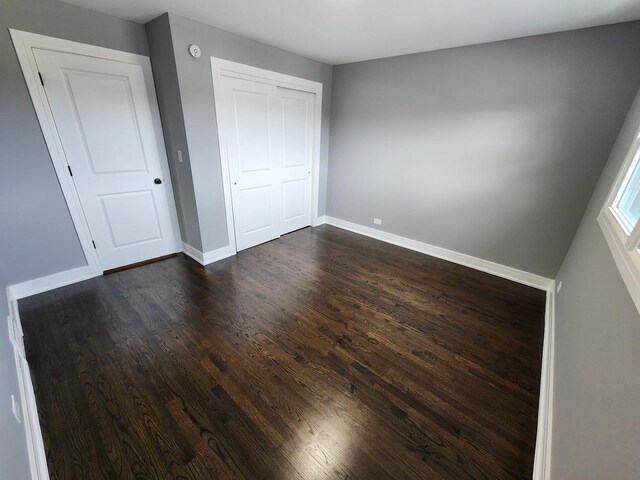 unfurnished bedroom with dark wood-type flooring, baseboards, and a closet