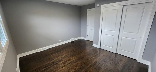 unfurnished bedroom with dark wood finished floors, visible vents, baseboards, and a closet