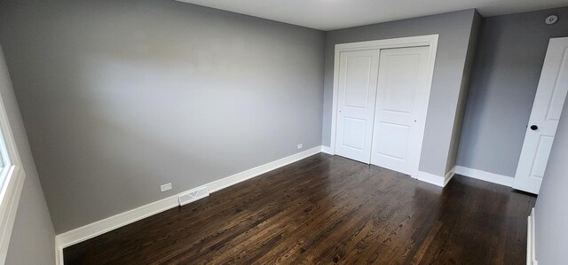 unfurnished bedroom with a closet, baseboards, and dark wood-style flooring