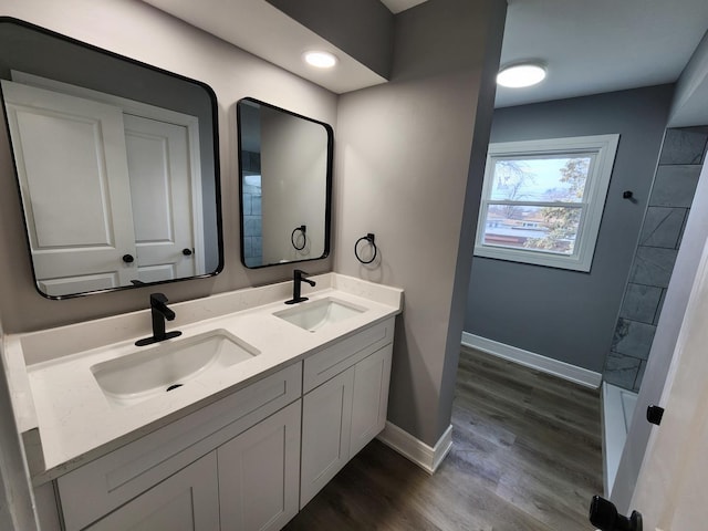 full bath featuring double vanity, wood finished floors, baseboards, and a sink