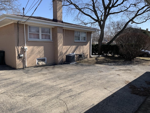 view of side of home featuring a patio, brick siding, central AC unit, and a chimney