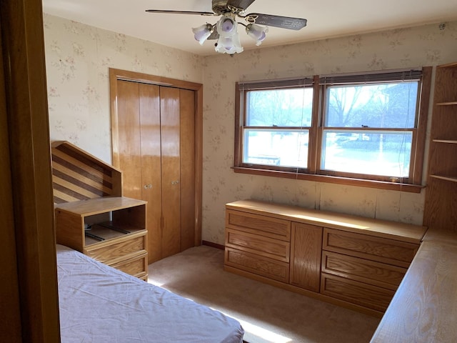 bedroom with wallpapered walls, ceiling fan, a closet, and light carpet