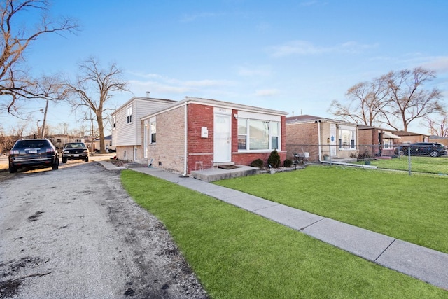 view of front of house with driveway, brick siding, a front lawn, and fence