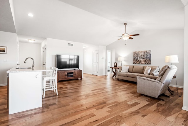 living area with visible vents, light wood-type flooring, baseboards, and vaulted ceiling