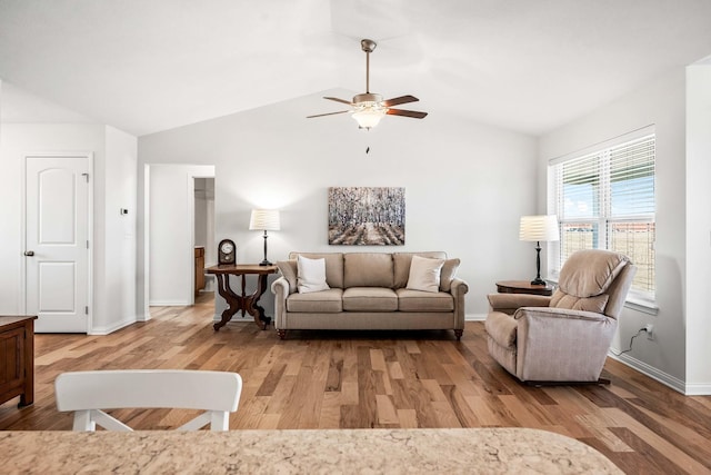 living area with light wood-type flooring, baseboards, ceiling fan, and vaulted ceiling