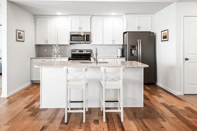 kitchen featuring a kitchen island with sink, a sink, light wood-style floors, appliances with stainless steel finishes, and decorative backsplash