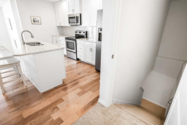 kitchen with a sink, decorative backsplash, light wood-type flooring, and stainless steel appliances