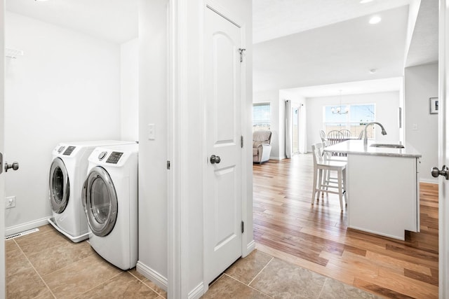 laundry room with laundry area, an inviting chandelier, a sink, light wood-type flooring, and washer and clothes dryer