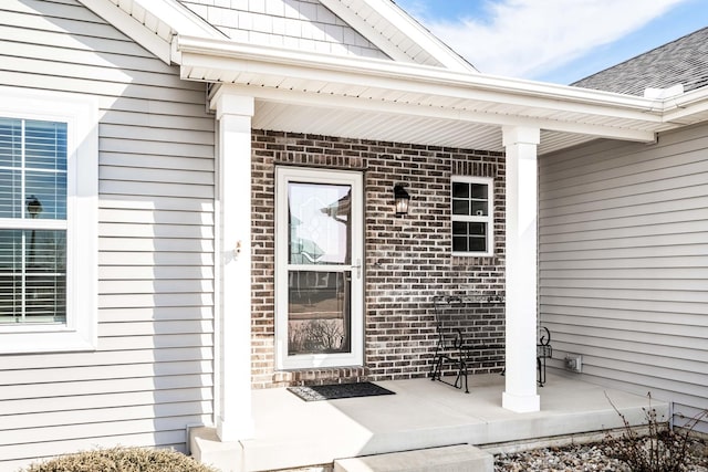 view of exterior entry with a porch, brick siding, and roof with shingles