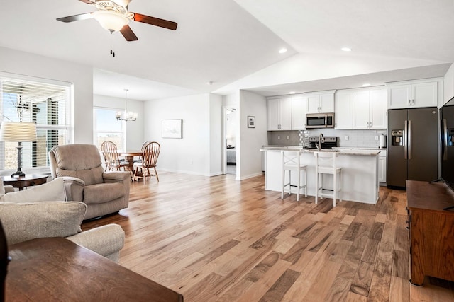 living area with baseboards, ceiling fan with notable chandelier, vaulted ceiling, and light wood finished floors