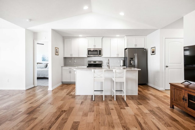 kitchen with a center island with sink, lofted ceiling, decorative backsplash, white cabinets, and stainless steel appliances