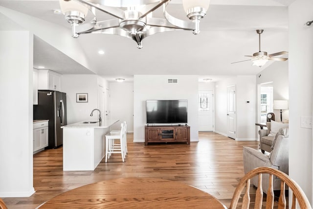 living area with visible vents, baseboards, lofted ceiling, ceiling fan with notable chandelier, and light wood-style floors