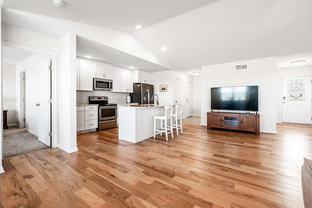 kitchen featuring visible vents, open floor plan, vaulted ceiling, appliances with stainless steel finishes, and white cabinets