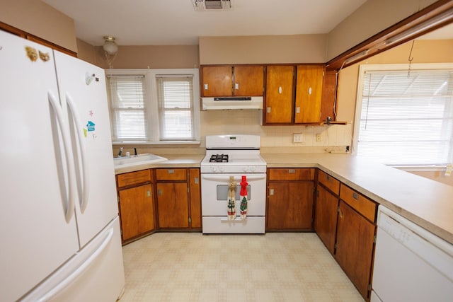 kitchen with under cabinet range hood, light floors, light countertops, brown cabinets, and white appliances