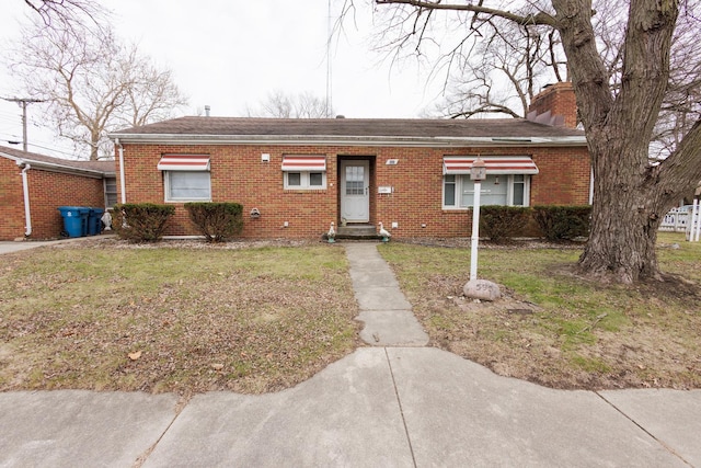 single story home featuring brick siding, a chimney, and a front yard