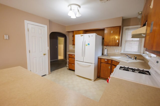 kitchen featuring under cabinet range hood, white appliances, arched walkways, and brown cabinetry