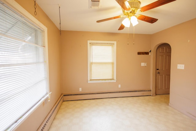 spare room with a baseboard heating unit, visible vents, arched walkways, and a wealth of natural light