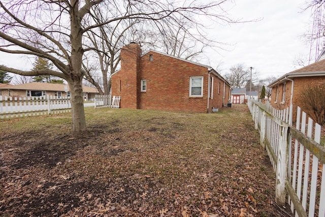 view of home's exterior with a yard, fence private yard, brick siding, and a chimney