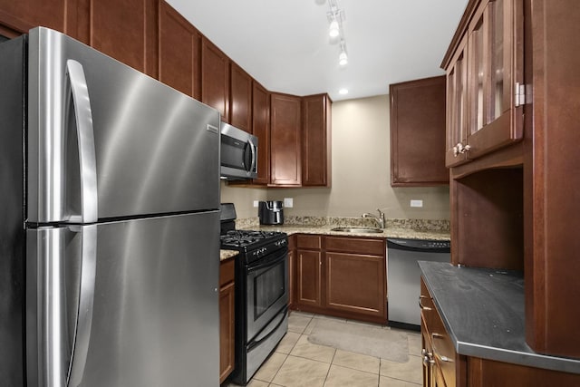 kitchen featuring light tile patterned floors, stone countertops, a sink, track lighting, and appliances with stainless steel finishes