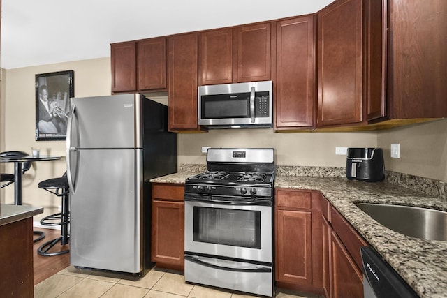 kitchen featuring a sink, light stone counters, light tile patterned floors, and stainless steel appliances