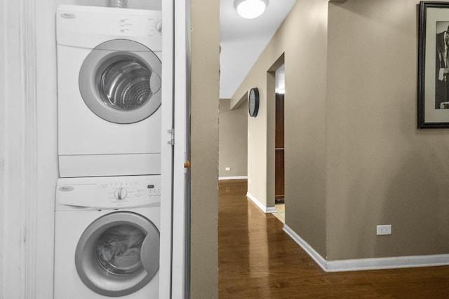 laundry room with dark wood finished floors, laundry area, baseboards, and stacked washing maching and dryer