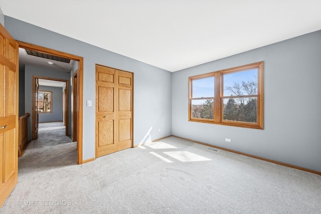 unfurnished bedroom featuring visible vents, multiple windows, light colored carpet, and baseboards