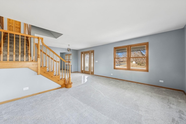 unfurnished living room featuring stairway, a healthy amount of sunlight, baseboards, and carpet floors