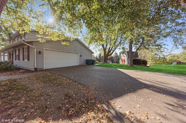 view of side of home with aphalt driveway, an attached garage, and a lawn