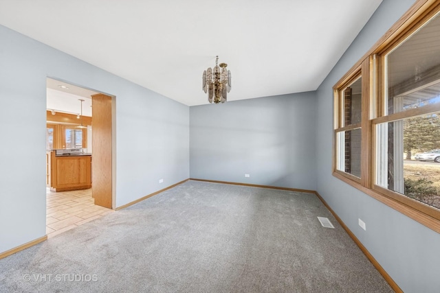 empty room with light carpet, a notable chandelier, plenty of natural light, and visible vents