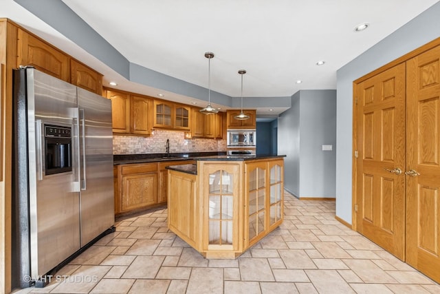 kitchen with tasteful backsplash, dark countertops, stainless steel appliances, brown cabinetry, and glass insert cabinets