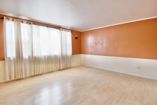 spare room with wainscoting, crown molding, and wood finished floors