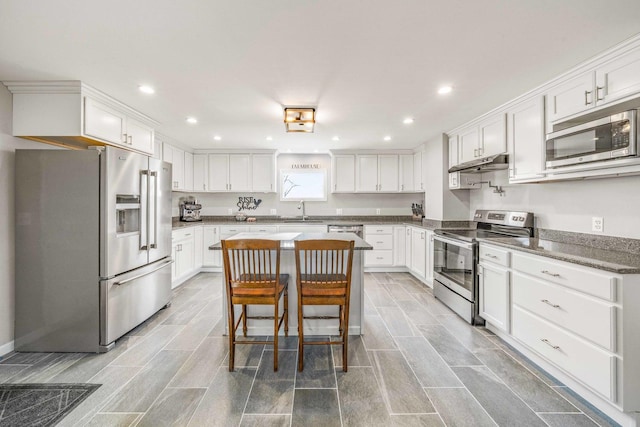 kitchen with under cabinet range hood, a kitchen island, appliances with stainless steel finishes, and white cabinets