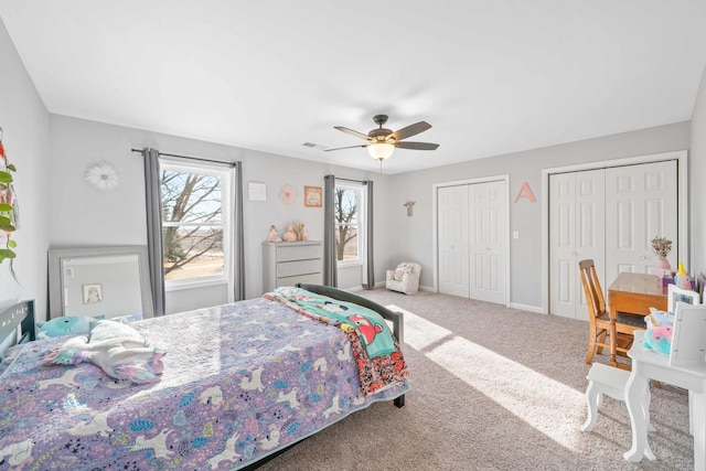 bedroom with a ceiling fan, visible vents, baseboards, multiple closets, and carpet flooring