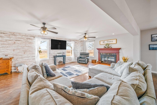 living area with baseboards, wood finished floors, a glass covered fireplace, and a ceiling fan