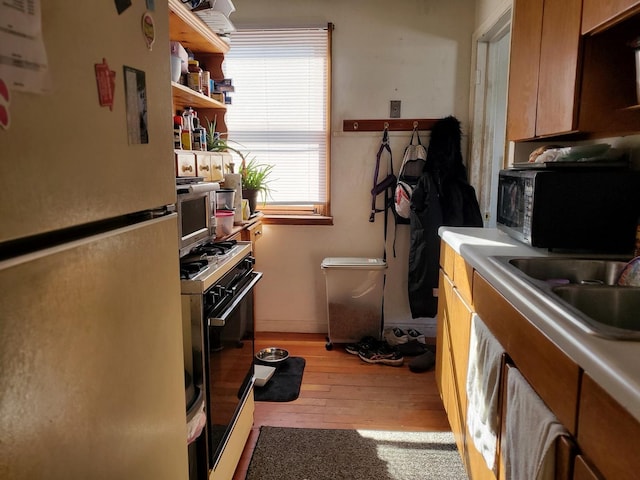 kitchen with light wood finished floors, range with gas cooktop, black microwave, light countertops, and freestanding refrigerator